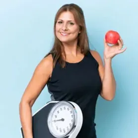 A woman, wearing a white robe, smiles while gently touching her face; she is in a brightly lit bathroom.